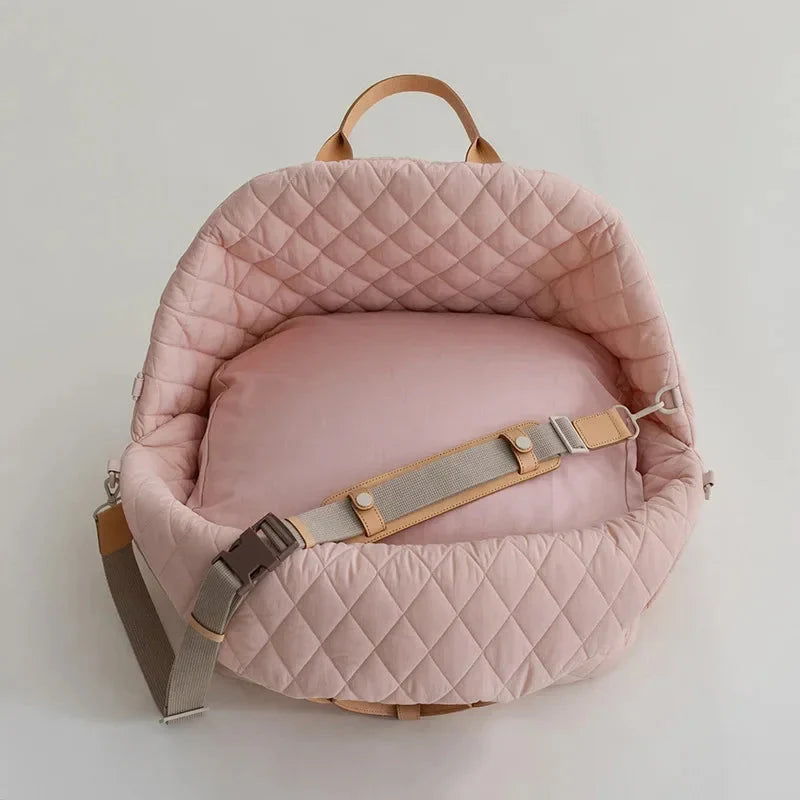 Pink quilted baby carrier with brown straps on a light gray background