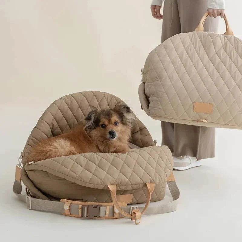 Dog lying in a beige quilted pet carrier with a person holding another similar carrier in the background.